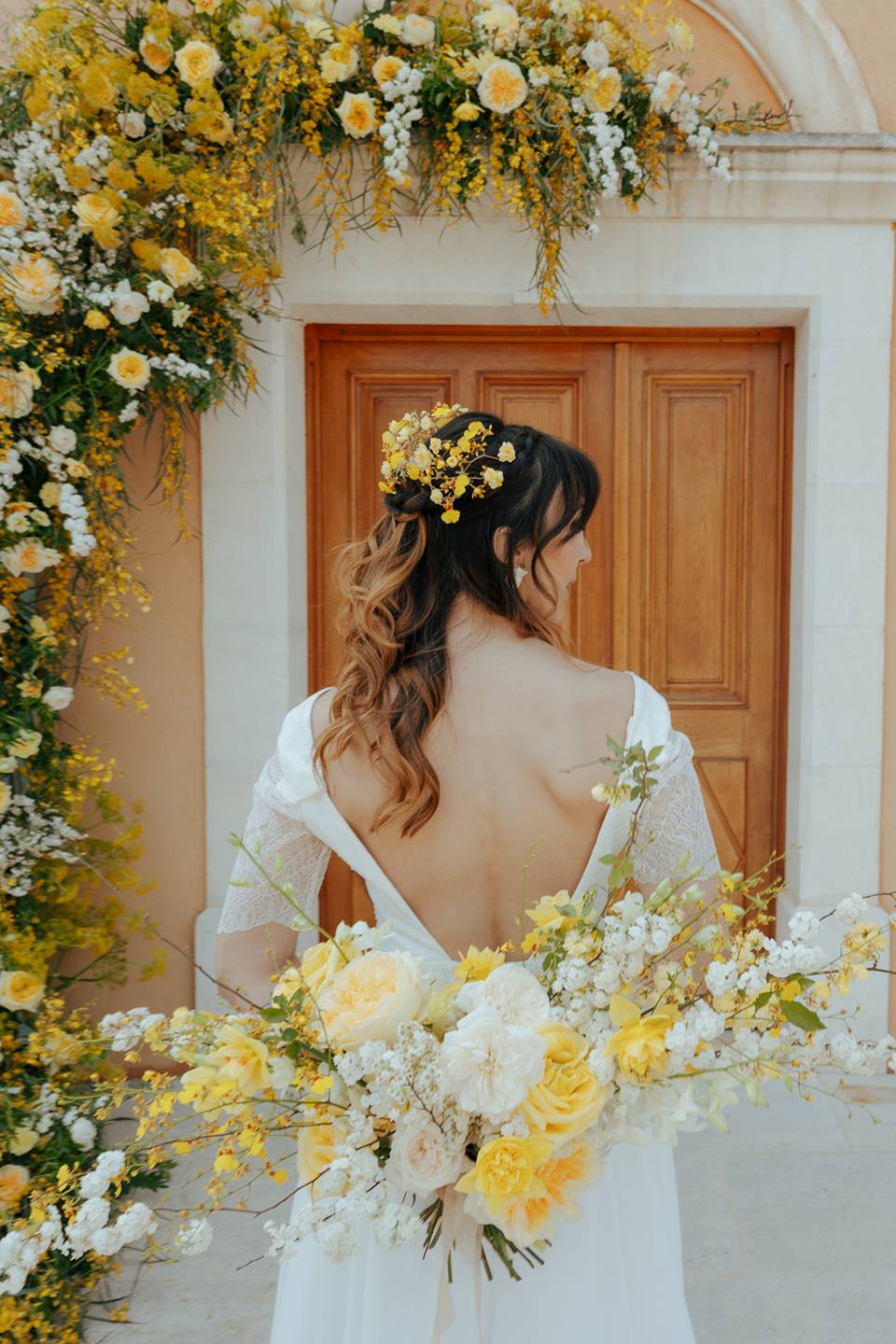 Mariée de dos avec un bouquet de fleurs blanches et jaunes